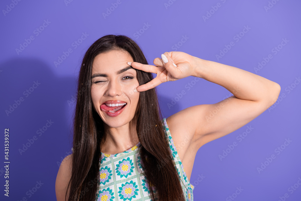 Obraz premium Young woman winking and playfully posing in front of a vibrant purple background, making a peace sign with her hand, exuding charm and fun