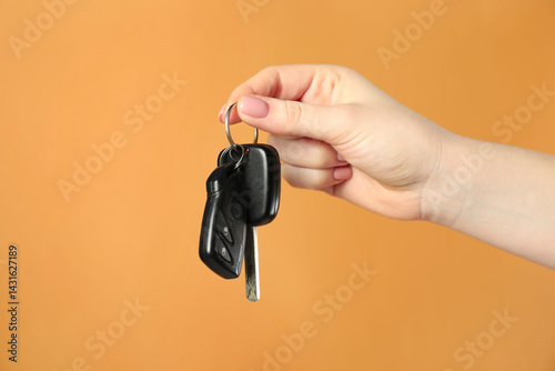 Woman with car keys on orange background, closeup