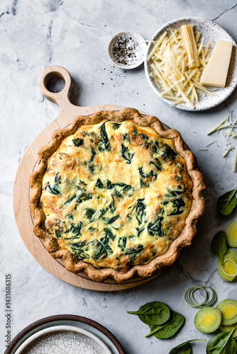 A delicious spinach quiche with a golden crust, served on a wooden board alongside fresh ingredients like spinach and cheese.
