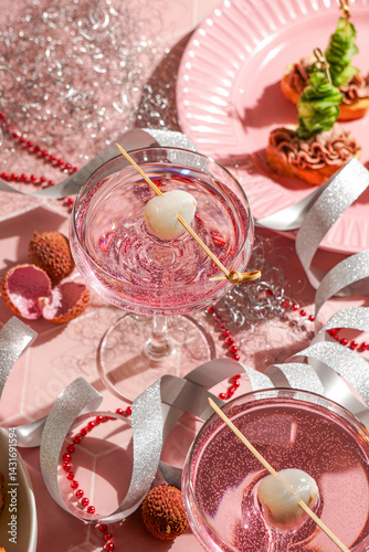 festive New Year table setting, two pink cocktails garnished with lychee and appetizers, red beads, silver ribbons, sparkly ornaments, for Christmas parties