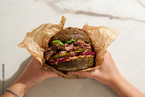 gourmet Roast Beef Sandwich, fresh lettuce, pickles, red onion, held person's hands, with a neutral background and hash sun lighting