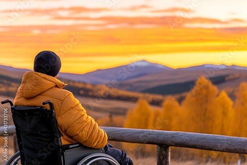 A man in a wheelchair enjoys the view of a mountain range at sunset