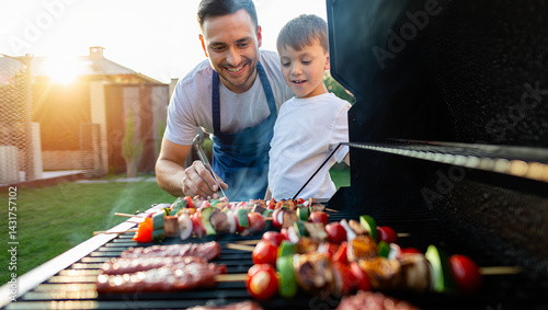 A father and son enjoy grilling kebabs together in their backyard during sunset. They share smiles and laughter as they prepare a delicious meal.