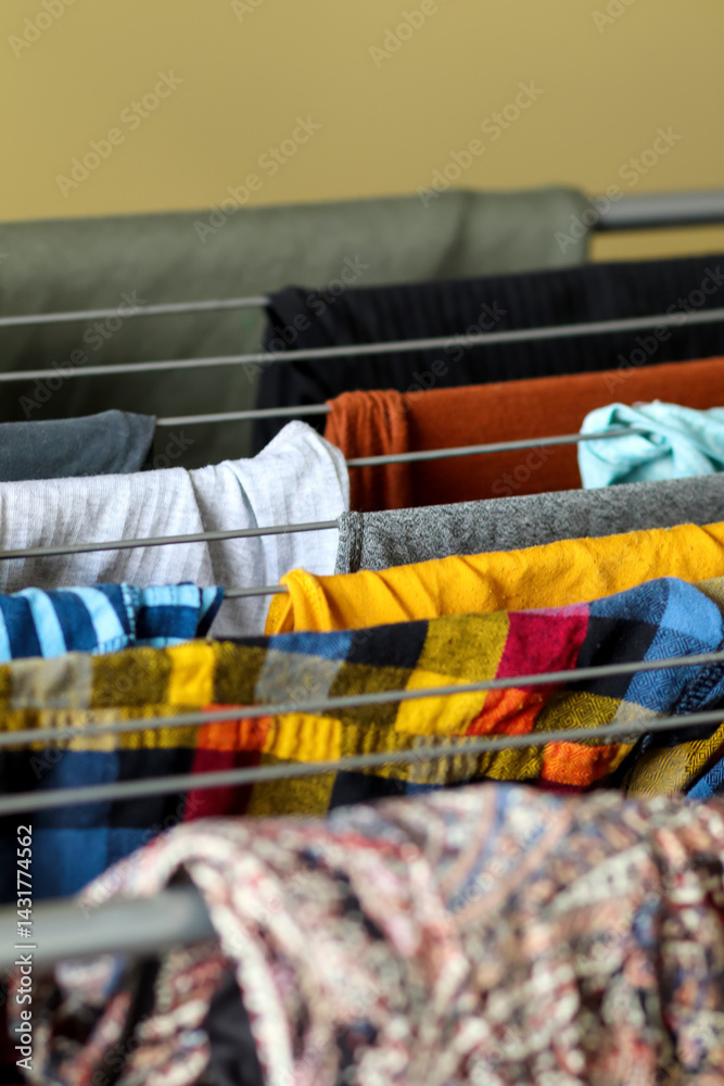 Yellow clothes drying on a metal folding rack, close-up shot with a clean background, vertical format, concept of laundry, dry, and home routine