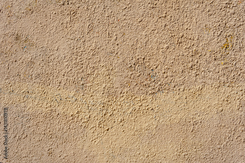 A yellow wall covered with numerous layers of plaster and paint. The layers form small irregularities and bumps.