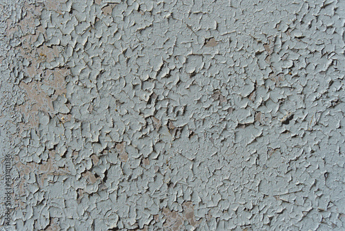 A wall with peeling paint. The paint is light blue and the wall is grey.