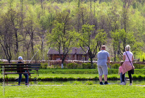 Obraz na płótnie A family fishing on the shore of a lake seen from behind w salonie