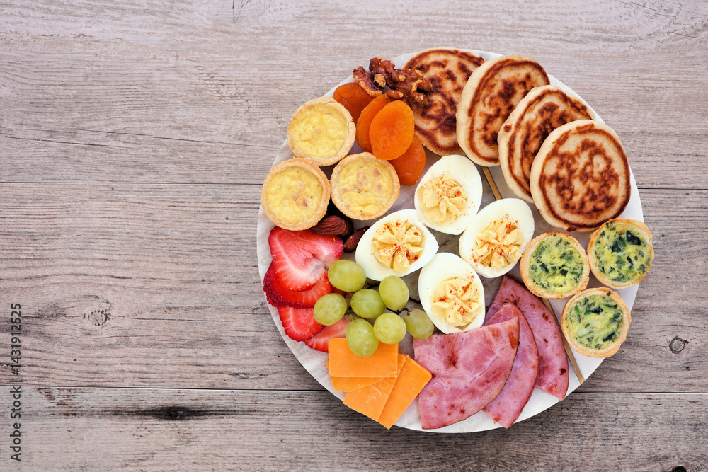 Breakfast or brunch grazing board. Assorted items including fruit, ham, quiche, pancakes and eggs. Top view on a wood background.