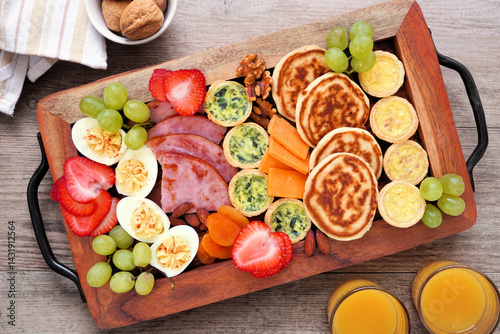 Obraz na płótnie Breakfast or brunch grazing board on a wood tray. Variety of items including fruit, ham, quiche, pancakes and eggs. Top view over a wood table background. w salonie