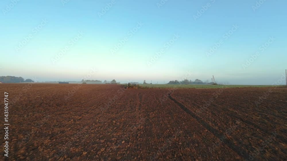 Drone aerial view of freshly plowed brown soil field with tractor marks at sunrise under clear blue sky, symbolizing agricultural preparation, rural development, and early morning farming activity Drone aerial view of freshly plowed brown soil field with tractor marks at sunrise under clear blue sky, symbolizing agricultural preparation, rural development, and early morning farming activity