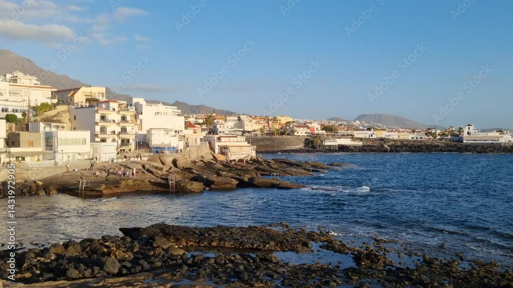 A relaxing view of Tenerife's bay with a yacht gliding across the calm ocean, a charming beach town along the coast, and the impressive Teide volcano in the distance. A relaxing view of Tenerife's bay with a yacht gliding across the calm ocean, a charming beach town along the coast, and the impressive Teide volcano in the distance.