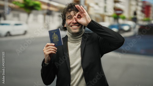 Hispanic man outdoors in a city holding a canadian passport, making an okay gesture in front of his eye, expressing happiness and travel excitement.