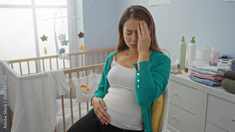 Pregnant woman sitting on a chair in a bedroom holding her head with a worried expression near a cradle surrounded by baby clothes in a cozy home nursery environment