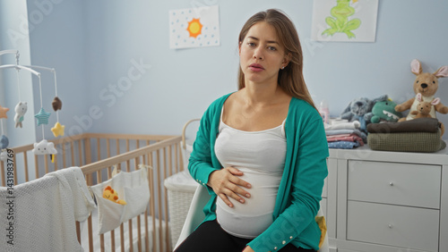 Obraz na płótnie Pregnant woman sitting thoughtfully on a bed in a stylish nursery room with a cozy atmosphere, surrounded by baby essentials, art, and soothing pastel tones. w salonie