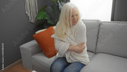 Obraz na płótnie Woman with albinism sitting in a cozy living room wrapped in a blanket, feeling cold, surrounded by soft pillows on a sofa, showcasing indoor comfort and warmth. w salonie