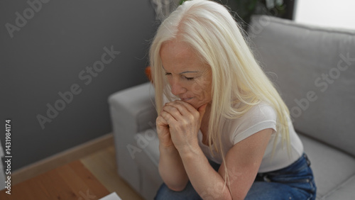 Woman with albinism sitting thoughtfully in a cozy living room, her hands clasped, exuding contemplation and emotion in a serene apartment setting.