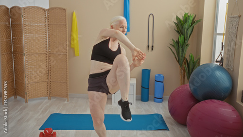Woman exercising in a gym with albinism performing a dynamic martial arts move surrounded by fitness equipment, showcasing strength, agility, and empowerment in an indoor setting.