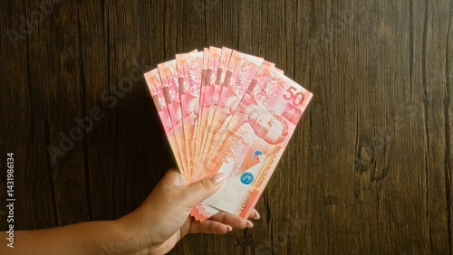 Obraz na płótnie Woman holding multiple philippine peso bills against a rustic wood background, showcasing currency notes in her hand with fingers visible. w salonie