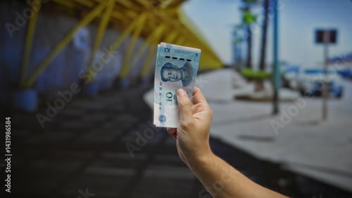 Obraz na płótnie Hand holding chinese yuan banknotes outdoors in urban city street setting suggesting business transaction or financial exchange context with male presence implied. w salonie