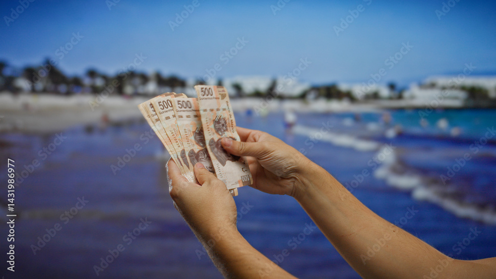 Hands holding mexican banknotes in a seaside setting, with a focus on investment and currency in a beachside town environment during a sunny vacation.