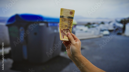Obraz na płótnie Hand of man holding hungarian forint banknotes outdoors near garbage container on city street in recycling location, suggesting economic themes in an urban environment. w salonie