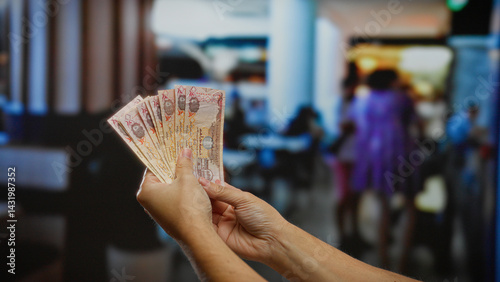 Man holding uae dirham banknotes indoors in a bustling coffee shop with blurred background, implying business transactions or financial planning context.