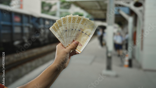 Man holding danish krone banknotes at an outdoor train station, showcasing the local currency in a public railway setting, emphasizing travel and financial concepts.