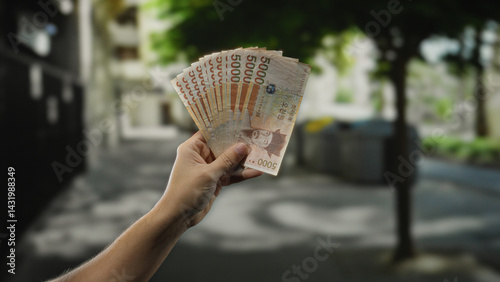 Obraz na płótnie Man holding south korean won banknotes in his hand outdoors on a bustling city street, capturing the essence of urban life and financial transactions in a vibrant setting. w salonie