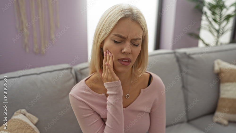 Woman holding cheek in pain sitting on a couch in a cozy living room with purple walls, showcasing a stylish and modern home interior with natural light.