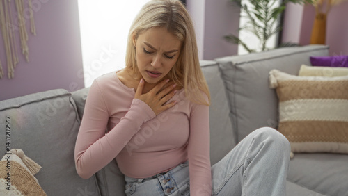 Woman sitting on a sofa in a cozy living room appears distressed, clutching her throat, surrounded by soft pillows and modern decor, with natural light filtering into the room.