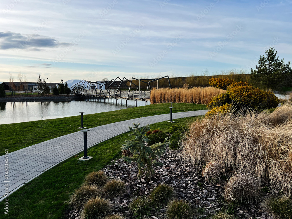 Obraz premium Beautiful landscaped park with wooden bridge over calm reflective water in daylight