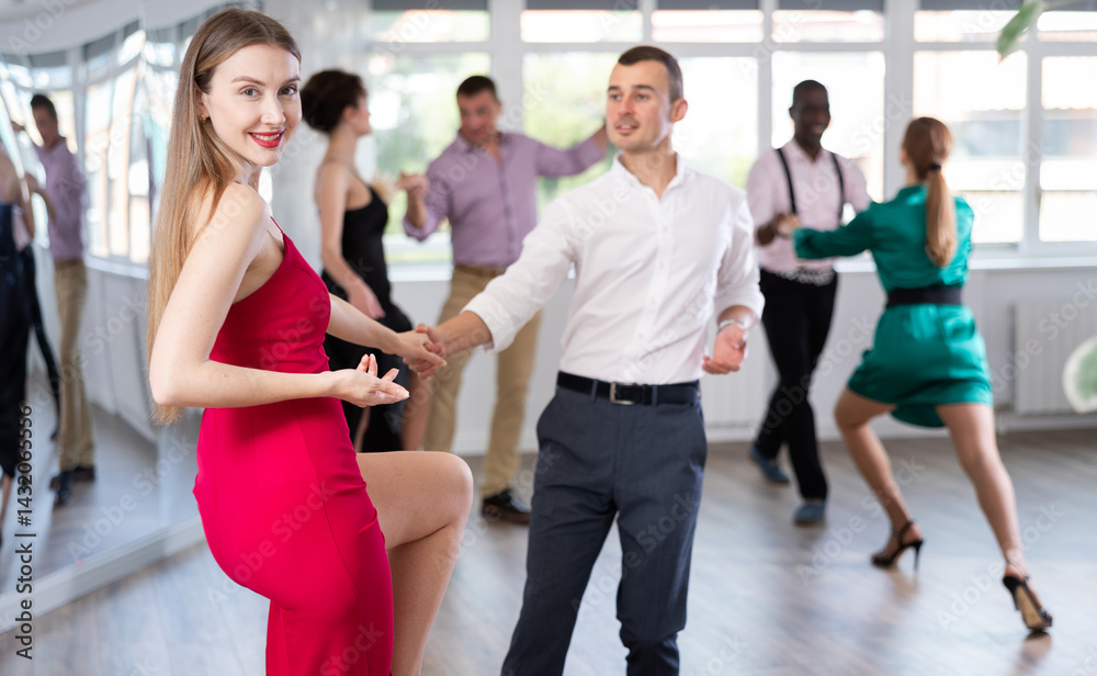 Fototapeta premium Smiling lady and man training swing dance in pair in dance-hall during dancing classes