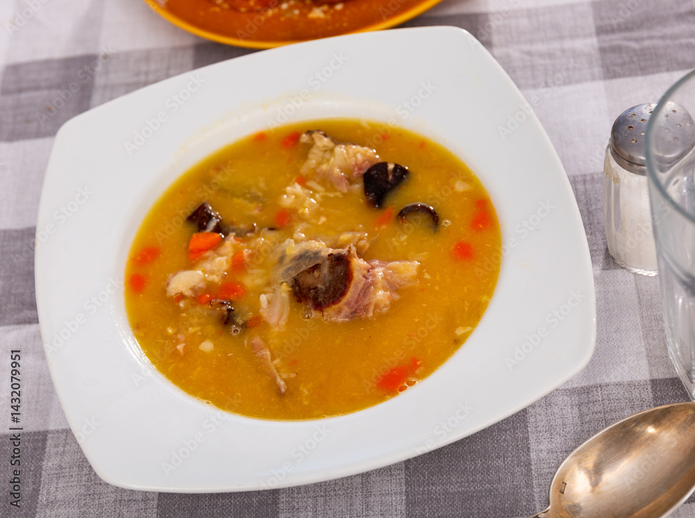 Plate of hearty pea soup with smoked meat served with bread