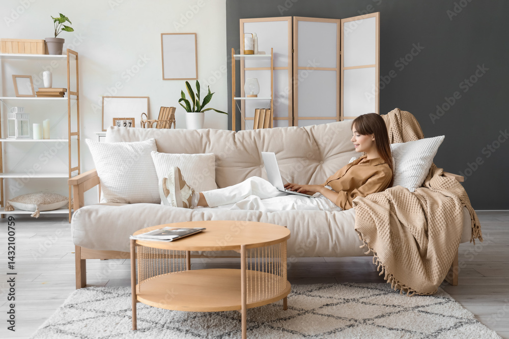 Pretty young woman with laptop relaxing on sofa