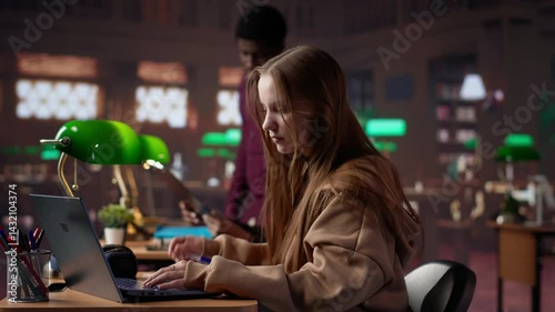 College student captivated by literature assignment at the academic library on campus, working on bachelor degree paperwork. Uses primary source materials from the database. Camera A.
