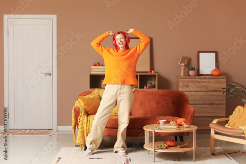 Young happy woman in headphones dancing and listening music at home