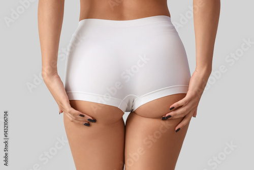 Young woman in underwear with cellulite problem on light background, back view