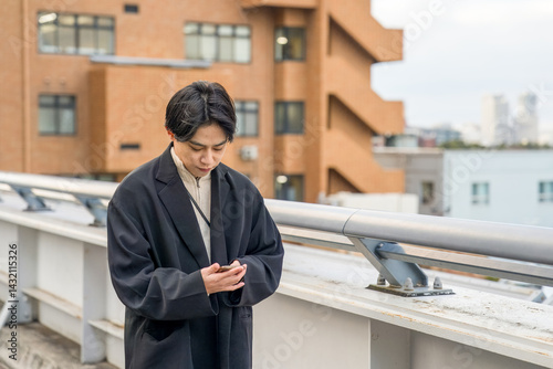 Obraz na płótnie A Japanese man in his twenties wearing a black jacket walks along a seaside path in Minato Mirai, Yokohama, Kanagawa Prefecture, enjoying the breeze, city buildings, and the calm harbor atmosphere. w salonie