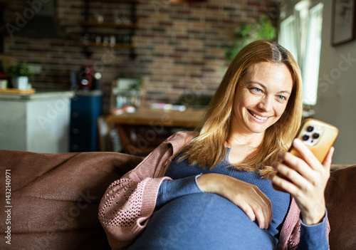 Pregnant woman using mobile banking app while relaxing on couch