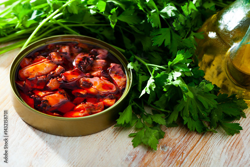 Natural Humboldt squid tentacles in Galician sauce in open tin can with herbs and oil on wooden table. Pacific seafoods