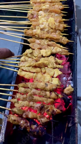 Hand movement turning the skewers in the process of grilling chicken satay, satay is made from chicken meat that is cut into small pieces then skewered on skewers, and grilled over hot coals