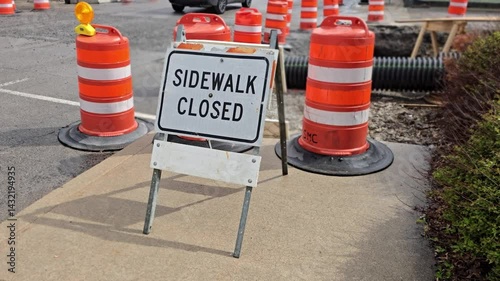 Sidewalk closed sign blocking off a cement walking path for maintenance and repair on a sunny bright day with city street landscape background