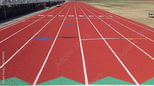 White starting line of a red running track at a school stadium on a bright sunny day with forest landscape background