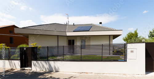 House with white roof and solar panel on top. The house is surrounded by fence and has mailbox on side