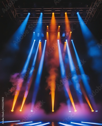Vibrant stage lights in blue and orange beams shining through fog on dark concert stage, creating a dramatic atmosphere for entertainment, events, or performances


