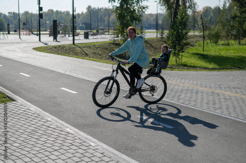 Obraz premium Caucasian woman riding a bicycle with her toddler son sitting behind her in a child seat.