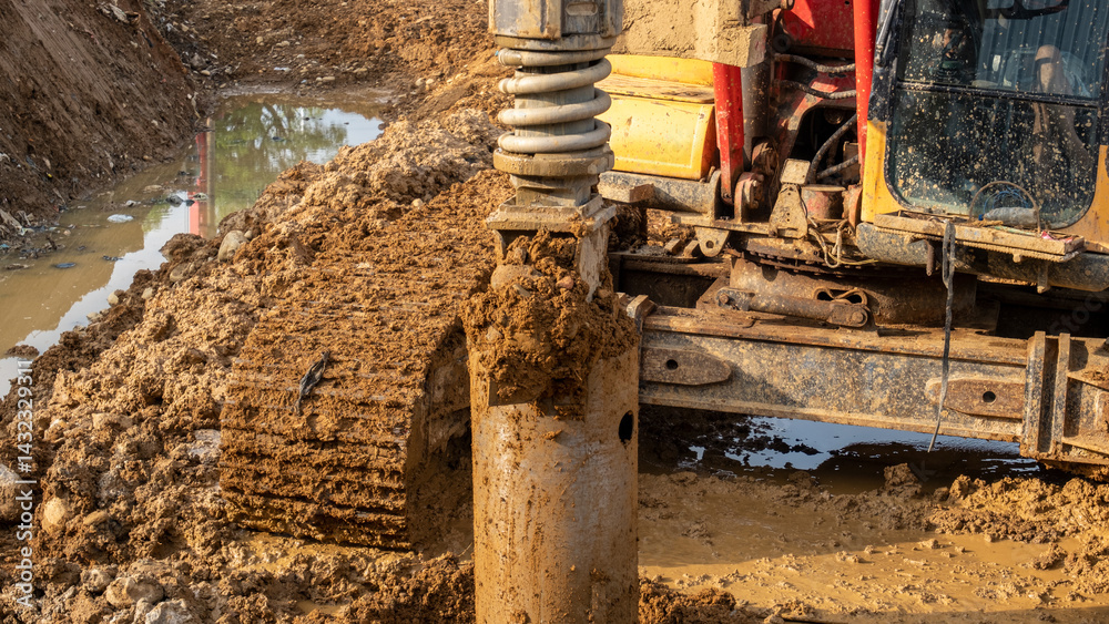 Αυτοκόλλητο Pile driving machine in action at a muddy construction site, showing hydraulic pressure system and tracked vehicle working on wet terrain for foundation reinforcement