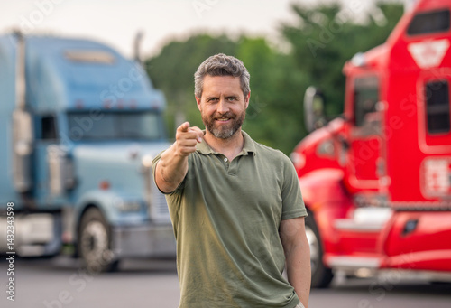 Handsome man driver in front of truck. Trucking owner. Truck driver. Man trucker driver near lorry truck. Transportation vehicles. Semi trucks vehicle. Hispanic man trucker point finger
