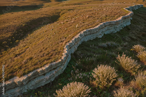 Windswept dry cliffside grassland curving dramatically toward sharp stratified edge above shadowed rocky sea escarpment