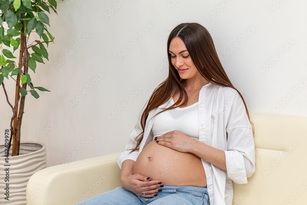 Happy pregnant woman gently touching her belly, sitting on sofa in a cozy home, showing maternal love and anticipation. Captures love, care, and connection during pregnancy. High quality photo